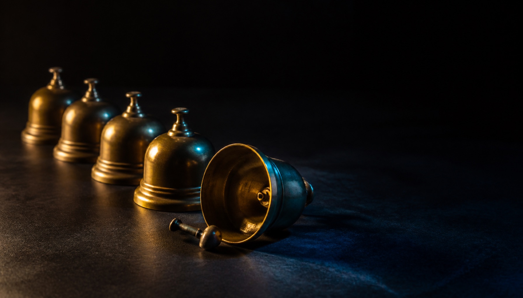 A row of brass service bells standing in line with one knocked onto its side and its clapper loose beside it