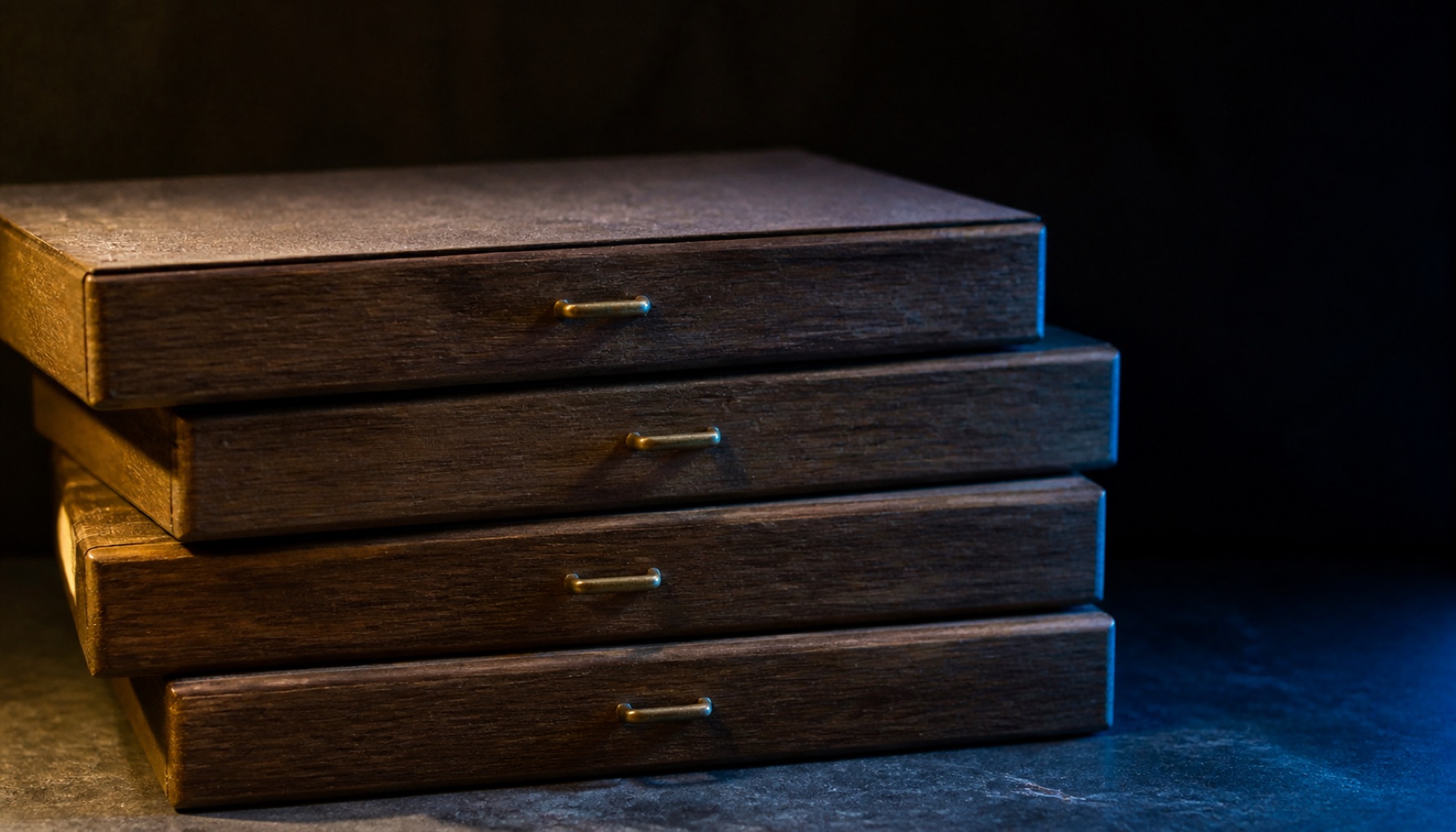 Four identical closed card-index drawers stacked slightly out of alignment with brass pulls and dust on the top surface